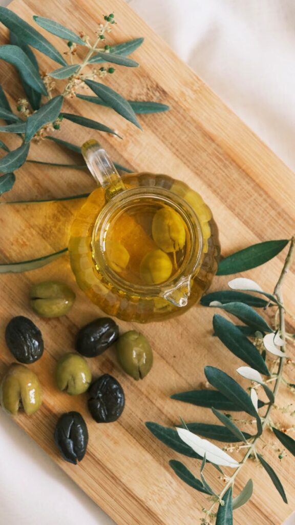 pexels-photo-25745497 A top view of a cruet with olive oil and olives on a wooden cutting board.